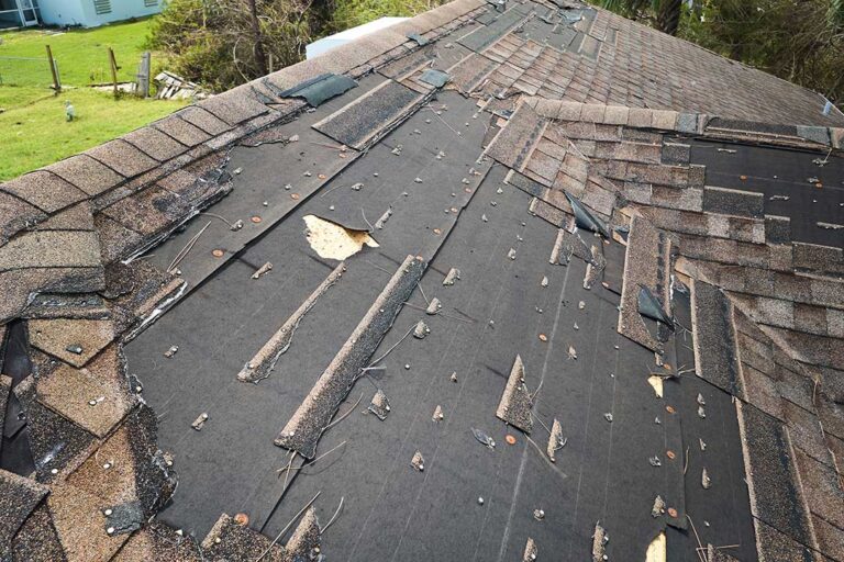 A homeowner examines a residential roof for missing shingles and gutter debris on a clear day.