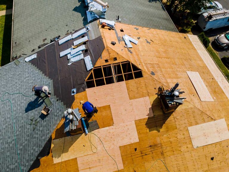 Homeowner examining loose shingles and damaged flashing beside a roof ladder after a storm.