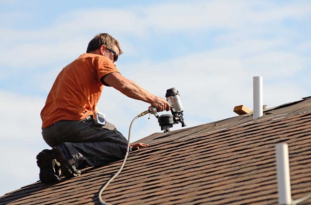 Workers secure a temporary roof covering beside renovation materials on a suburban home.