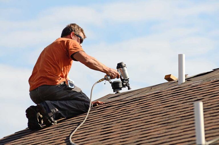 Workers secure a temporary roof covering beside renovation materials on a suburban home.