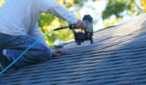 Workers remove old shingles from a residential roof while protective coverings shield landscaping below.